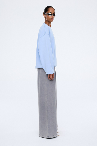 A medium close-up, three-quarter studio shot focusing on the upper torso and details of the soft blue sweater. The model is wearing sleek silver metallic sunglasses, highlighting the intricate texture of the white 3D script chest embroidery and additional white "EP Studios" embroidered detailing near the lower ribbed hemline.