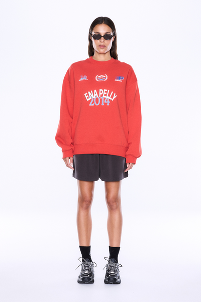 Full-length front view of a model wearing the relaxed-fit ENA PELLY Mila Oversized Sweater in Vintage Red with black shorts and sunglasses.