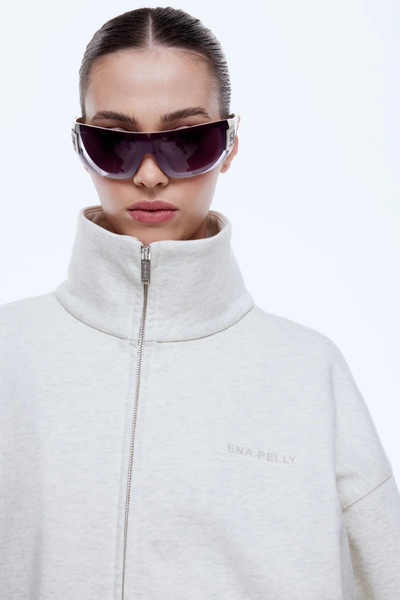 Close-up front shot of the ENA PELLY Paris Terry Zip Thru in Oat Marle, highlighting the high collar, metal two-way zipper, subtle tonal chest logo, and soft terry fleece texture.
