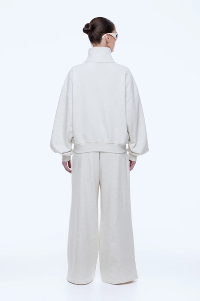 Full-length rear view of a model wearing the oversized ENA PELLY Paris Terry Zip Thru sweater in Oat Marle, featuring ribbed hem detailing and relaxed slouchy sleeves.