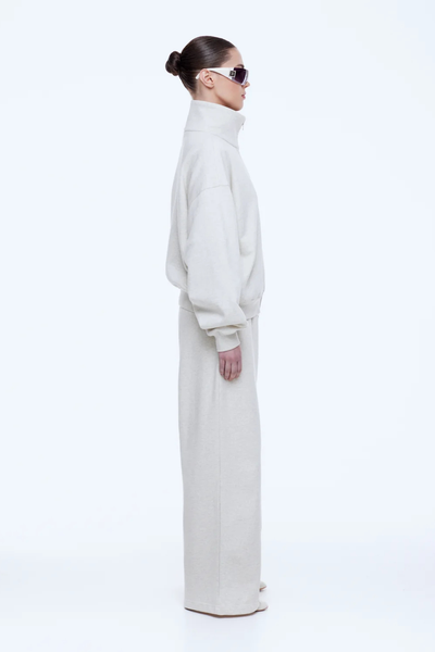 Full-length side profile shot of a model in the ENA PELLY Paris Terry Zip Thru in Oat Marle, showcasing the dropped shoulder design and relaxed off-duty silhouette.