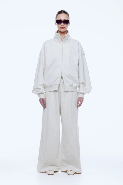 Full-length front shot of the ENA PELLY Paris Terry Zip Thru in Oat Marle unzipped slightly at the hem using the two-way silver zipper.