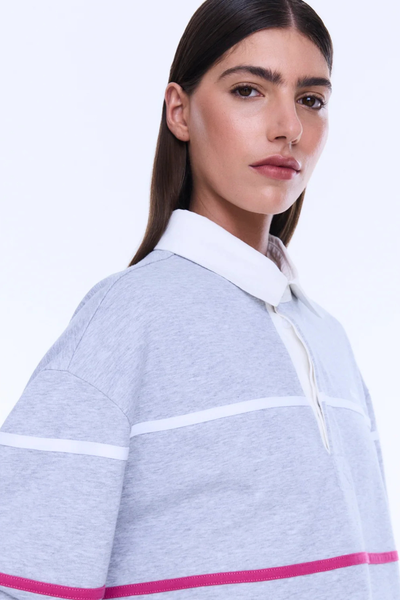 A full-length profile shot showing the side view of the model wearing the grey marle striped polo shirt. This perspective illustrates the relaxed drop-shoulder design, the long sleeves, the comfortable slouchy silhouette, and the small split at the side hem, paired with dark-wash wide-leg denim jeans.