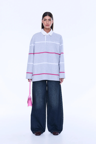 A full-length front view of the model standing straight while holding a small hot pink handbag. The image displays the complete long-sleeve silhouette of the grey marle polo, its contrast white collar, the embroidered Ena Pelly chest branding, and the full length of the matching dark wide-leg jeans.