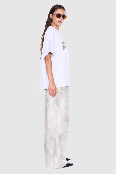 Studio side profile view of a model wearing a white marle short-sleeve cotton tee paired with wide-leg printed trousers.