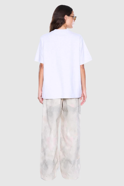 Studio rear view of a model showcasing the fit, crew neckline, and short sleeves of a white marle cotton t-shirt styled with loose pants.