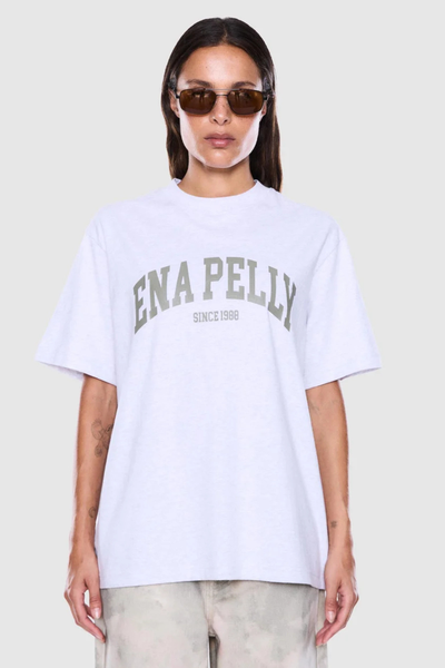 Studio front shot of a model wearing tint-lensed sunglasses and a white marle relaxed-fit short-sleeve t-shirt featuring an olive green collegiate "Ena Pelly" arched graphic across the chest.