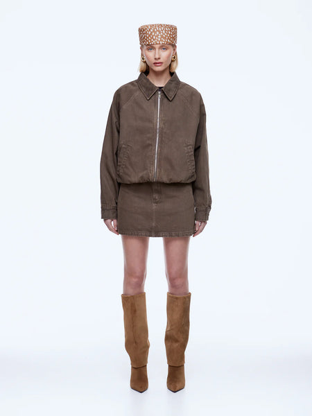 Full-length studio shot of a model showcasing the ENA PELLY Billy Denim Bomber Jacket in a vintage-inspired mushroom brown wash. The oversized cotton denim jacket is shown fully zipped, paired with a matching denim mini skirt, a patterned brown and white pillbox hat, and knee-high tan suede boots against a clean white backdrop.