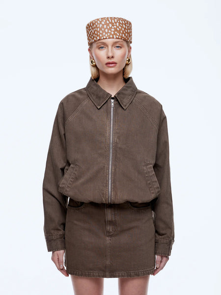 A three-quarter studio shot focusing on the upper body and details of the ENA PELLY Billy Denim Bomber Jacket in mushroom brown. The image highlights the classic collar, distinct raglan sleeve stitching, and the silver hardware of the two-way zipper closure.