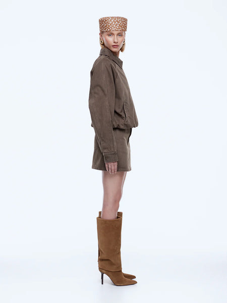 Side profile studio shot of a model wearing the ENA PELLY Billy Denim Bomber Jacket in mushroom. The photograph shows the jacket's generous silhouette, relaxed sleeves with gathered elastic cuffs, and the matching cotton denim skirt ensemble.