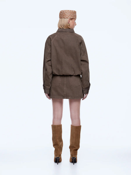 Full-length rear studio view of the model wearing the mushroom brown ENA PELLY Billy Denim Bomber Jacket. The shot displays the clean yoke lines, oversized fit, and slouchy volume created by the elasticated hemline, paired with a matching mini skirt and tall tan stiletto boots.