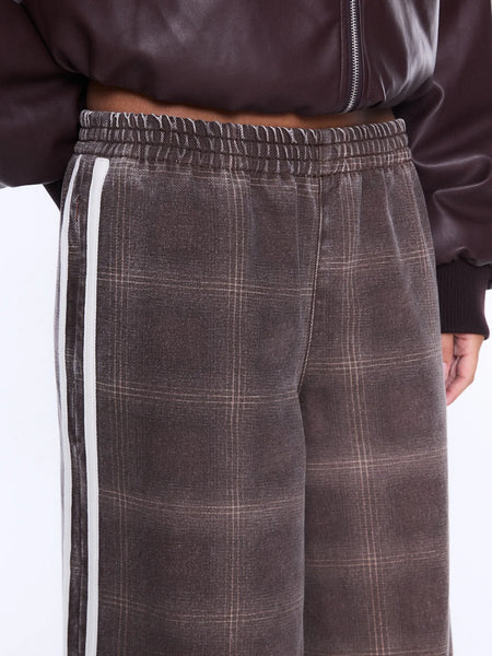A macro product detail shot showcasing the texture and upper waistline construction of the Myla Wide Leg Pant. The image highlights the detailed burgundy and beige checked print pattern, the gathers along the comfortable elasticated waistband, and the clean finish of the dual white racing stripes along the side.