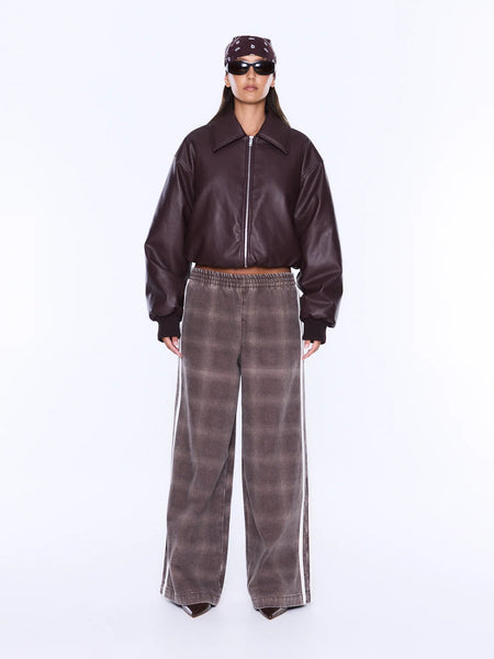 A front view studio shot focused on the lower half of a model wearing the ENA PELLY Myla Wide Leg Pant in Burgundy Check. The wide-leg pants feature an all-over muted plaid yardage print, an encased elastic waistband, and two striking white contrast stripes running down the side seams, paired with a dark cropped leather bomber jacket.