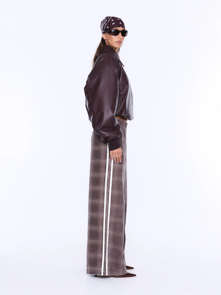 A full-length profile studio shot of a model showcasing the side silhouette of the Myla Wide Leg Pant. The image perfectly illustrates the relaxed, fluid drape of the wide legs and highlights the dual white contrast racing stripes extending from the elastic waistband down to the hem.