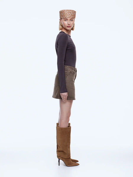 A full-length rear view studio shot of a model wearing the ENA PELLY Stella Denim Mini Skirt. The image emphasizes the high-waisted fit, two classic back patch pockets, and a signature black leather Ena Pelly brand patch on the right side of the waistband.