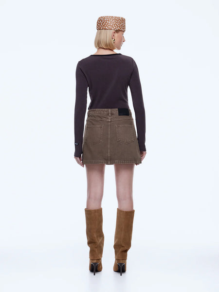 A full-length side profile studio shot of a model highlighting the vintage-inspired character and clean straight cut of the mushroom brown Stella Denim Mini Skirt. The outfit is styled with a fitted dark long-sleeve tee and stiletto heel suede boots.