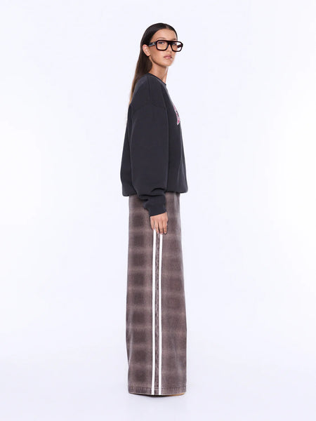 A model wearing a black crewneck sweatshirt and a brown wide-leg pleated skirt with a white side stripe, photographed against a plain white studio background.