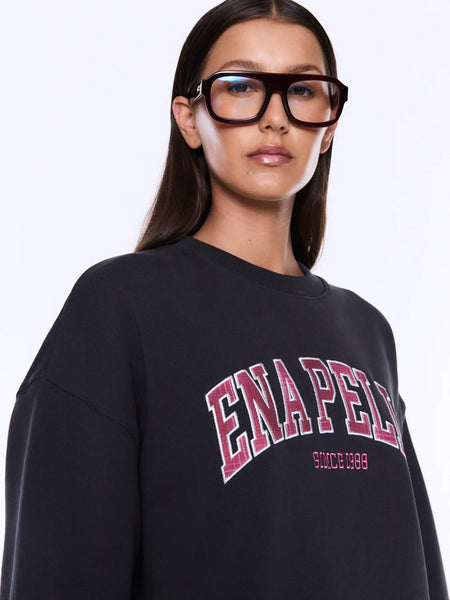 A close-up macro detail shot focusing on the high-quality collegiate chest graphic of the phantom black Mila Oversized Sweater. The shot displays the tactile burgundy plaid fabric insert appliqué and the fine contrast embroidery stitch details along the text boundaries.