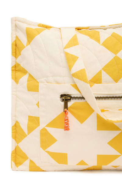 A close-up of the front external pocket, highlighting the antique brass metal zipper, orange paracord zip puller, and the intricate star-pattern quilting.
