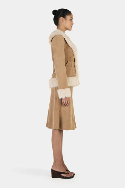 A side profile studio shot emphasizing the precise 60cm mid-length crop of the tan outerwear piece and the thick, plush volume of the cream faux fur lining the sleeves.