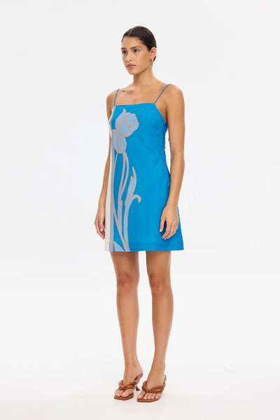 Three-quarter studio shot of a model wearing the KIVARI Fleur Mini Dress in Blue Ivory paired with tan mule sandals.