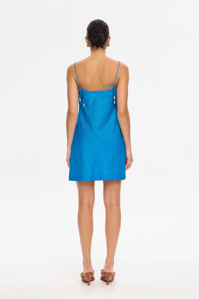 Back view of a model wearing the KIVARI Fleur Mini Dress in Blue Ivory, showing the straight back neckline, thin adjustable tie straps, and mini length.