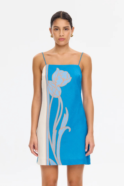 Medium studio portrait of a model wearing the KIVARI Fleur Mini Dress in Blue Ivory, showing the straight neckline and oversized floral placement print.