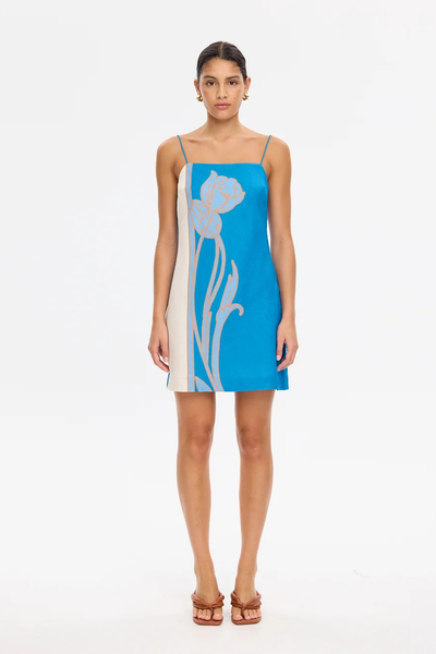 Studio full-length view of a model wearing the KIVARI Fleur Mini Dress in Blue Ivory featuring a straight neckline and bold floral motif.