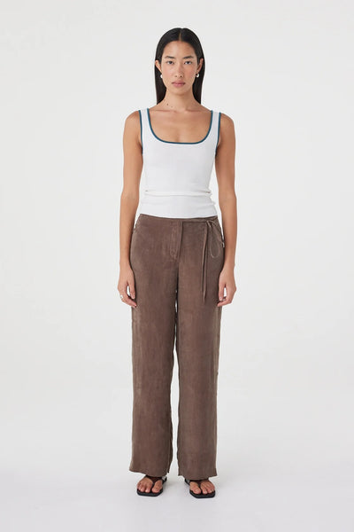 Full-body front studio view of a model wearing the Arcaa Movement Maisie Tie Pant in Espresso paired with a white ribbed tank top and dark sandals.