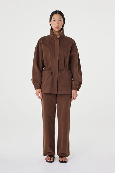 A full-length front studio shot of a model wearing the Arcaa Movement Amari Jacket in Espresso. The image highlights the relaxed, oversized silhouette, the gathered elasticated waist detail, and the matching espresso brown straight-leg trousers against a plain white background.