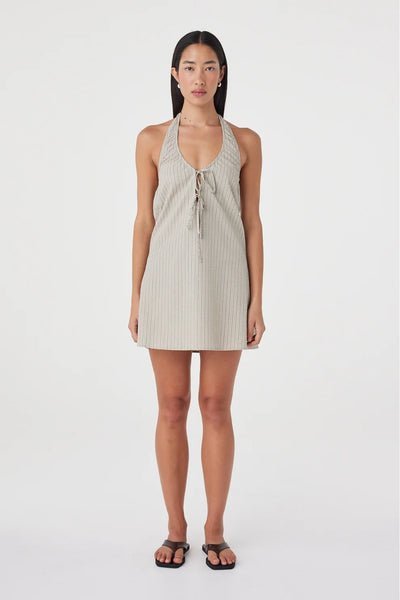 Full-length front studio view of a model wearing the Arcaa Movement Joni Mini Dress in Taupe Stripe featuring a halter neckline, double front ties, and an A-line mini silhouette, paired with dark flat sandals.