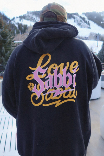 A full-length studio product shot from the back on a model wearing the Gimme Bear Hugs Hoodie, showcasing the large screen-printed statement graphic artwork across the back panel featuring bold typography and mountain-town illustrations in black and warm tones.