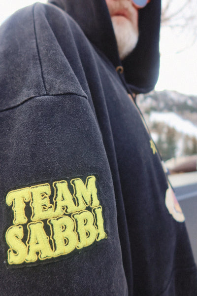 A macro studio close-up shot focusing on the high-quality screen print detail of the exclusive Sabbi teddy bear graphic on the front chest, emphasizing the textured finish of the cotton-polyester blend fleece fabric.