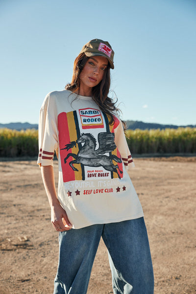 A dynamic, full-length outdoor lifestyle shot of a model walking in a rural country field, demonstrating the loose, fluid drape and extra-long length of the 100% cotton fabric, ideal for styling as a relaxed t-shirt dress.
