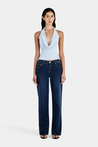 Full-length studio front view of a model wearing dark blue straight-leg jeans and a sky blue jersey halter top with a low draped cowl neck.