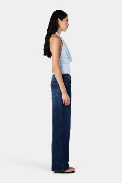 Studio side profile view of a model wearing dark denim jeans and a sky blue jersey halter neck top.