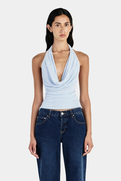 Studio mid-shot front view of a model wearing a light cornflower blue jersey halter top with a low draped cowl neck.
