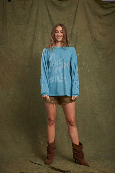Full-body studio shot of a model wearing the Kinga Csilla Paper Sun Roses Tee in Blue styled with frayed shorts and brown slouch boots.