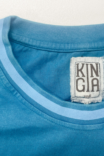 Close-up detail shot of the crew neck collar on the Kinga Csilla Paper Sun Roses Tee in Blue, featuring a light blue contrast trim and woven inner neck tag.