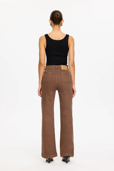 A full-length rear view of the studio model from behind, showcasing the clean back panel construction of the espresso brown jeans. The shot details the high-rise waist configuration, two symmetrical curved rear patch pockets with contrast topstitching, the tan Kivari leather back patch on the right waistband, and the full-length subtle flare at the hem.