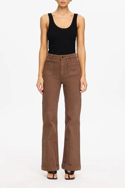 A full-length front view cropped below the chin, showing the model standing straight against a white backdrop. This image highlights the front technical details of the high-waisted 100% cotton denim, including the two prominent curved patch pockets, contrast stitching lines along the panels, a zip fly with a metal jean stud closure, and structured wide legs.