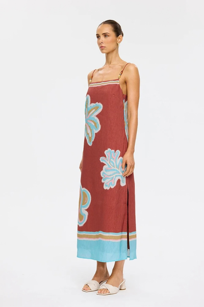 Studio side profile of a model wearing the maroon linen-viscose midi dress with oversized botanical placement prints in aqua, pink, and ochre, featuring a side slit and strappy heels.