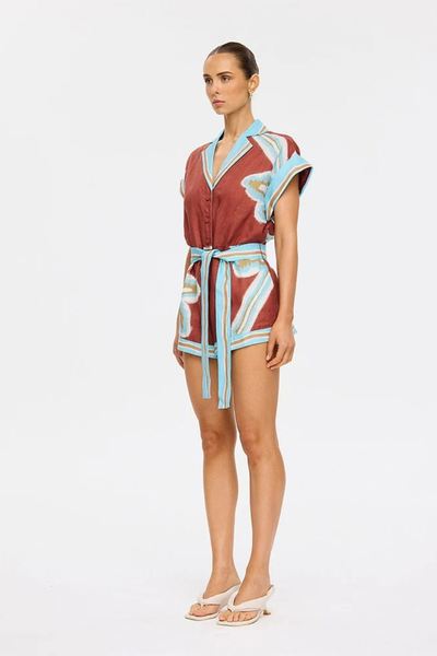 Studio side profile of a model wearing the maroon linen-cotton playsuit with contrast aqua trim, tile-inspired placement prints, and a tied waist belt.
