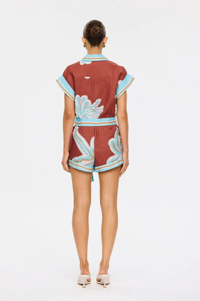 Studio rear view of a model standing in the maroon and aqua painterly-motif playsuit against a plain white background.