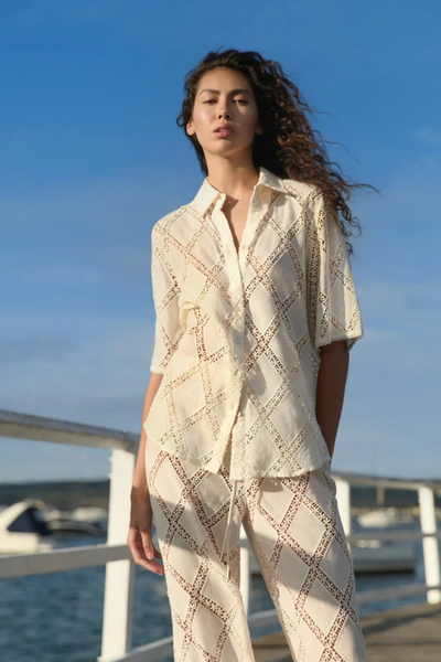 Outdoor medium shot of a model on a pier wearing the KIVARI Izzy Pant in Cream paired with the coordinating resort shirt.