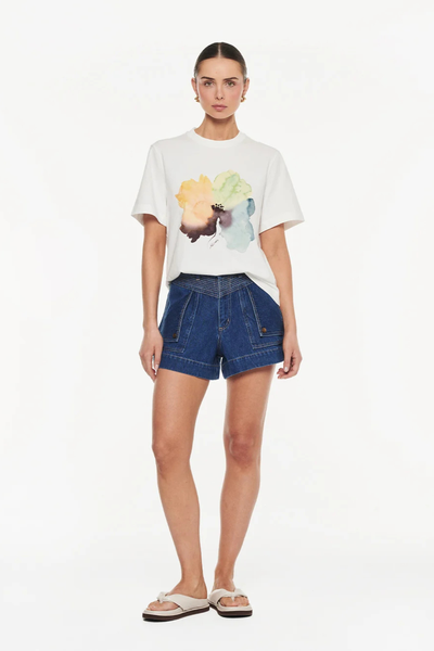 Full-length studio front view of a model wearing an ivory organic cotton graphic t-shirt slightly tucked into dark wash denim shorts.