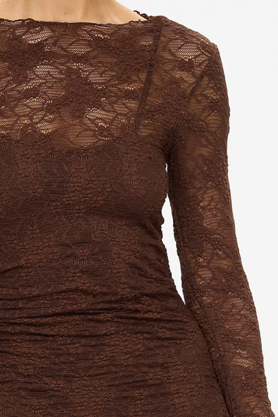 A macro close-up crop of the upper torso and neckline, focusing tightly on the intricate, semi-sheer floral pattern of the chocolate brown stretch lace. The shot illustrates the clean finish of the boat neckline and the layered silhouette of the matching thin-strap slip dress underneath.