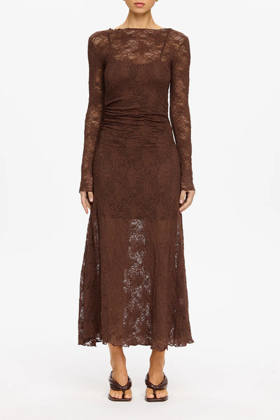 A cropped studio shot of the model from the nose down, standing straight with arms at her sides. This layout highlights the symmetry of the fitted bodice, the gathered ruching localized at the right waistline, the semi-sheer maxi length skirt overlay, and the square-toe dark brown kitten heels.