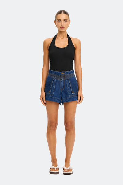 Full-length studio portrait of a model wearing the fitted Kivari Rhea Halter Top in Black with dark wash denim shorts and cream sandals against a plain background.