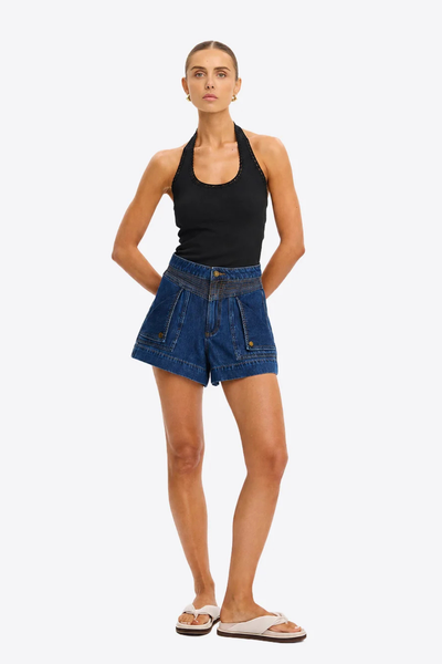 Full-length view of a model posing with hands behind her back in the Kivari Rhea Halter Top in Black and casual denim utility shorts.
